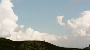 Film photo of a rolling hillside with plenty of negative space, featuring two people as silhouettes on a hill at the bottom of the frame