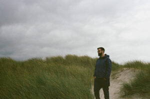 Film photo of a young man standing among the grass-covered sand dunes of Denmark