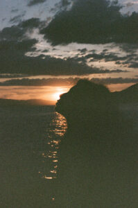 Film photo of the silhouette of a young woman standing in front of the setting sun