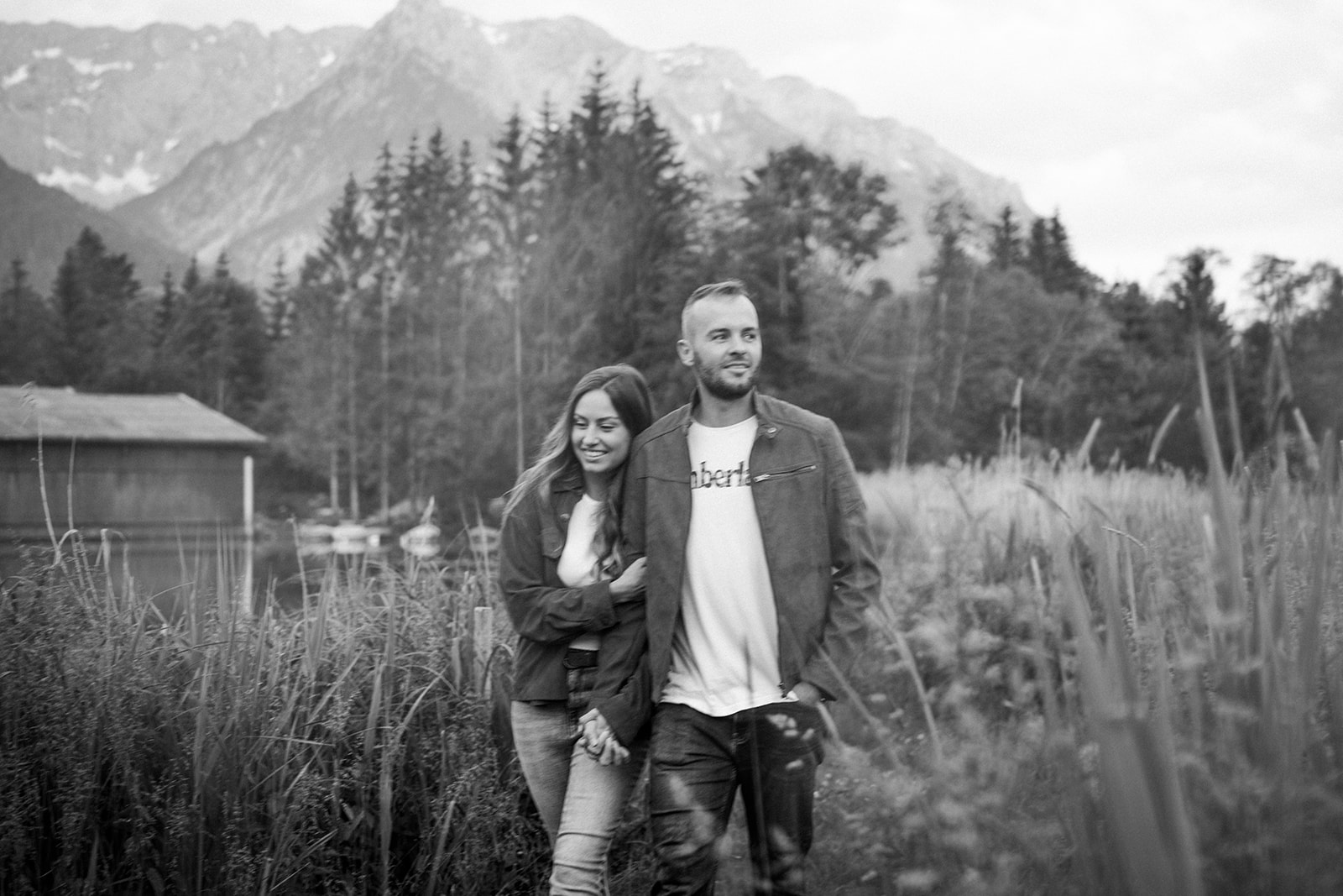 Black-and-white photo of a couple walking arm in arm through a meadow with the Wilder Kaiser in the background