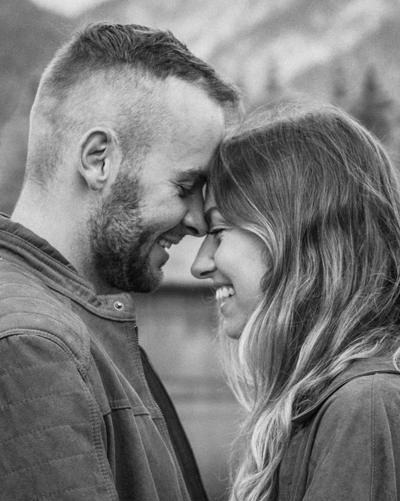 Intimate black-and-white photo of a couple touching foreheads and smiling at each other