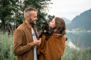 Young couple holding a black-and-brown spotted cat while smiling at each other
