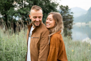 Young couple standing in tall grass while the woman rests her chin on his shoulder