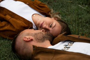 Couple lying on the ground smiling at each other, with focus on the woman