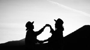 Schwarzweiß-Silhouette von zwei Schwestern mit Hüten vor Bergen und klarem Himmel