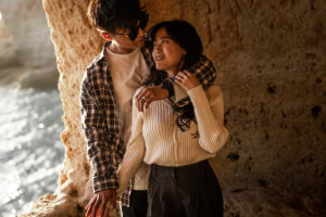 Young Korean couple standing arm in arm in a cave at the Algarve while looking lovingly at each other