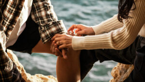 Close-up of hands holding each other with ocean waves in the background