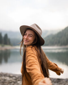 Portrait of photographer Caro by a lake, smiling while opening her arms and turning toward the camera