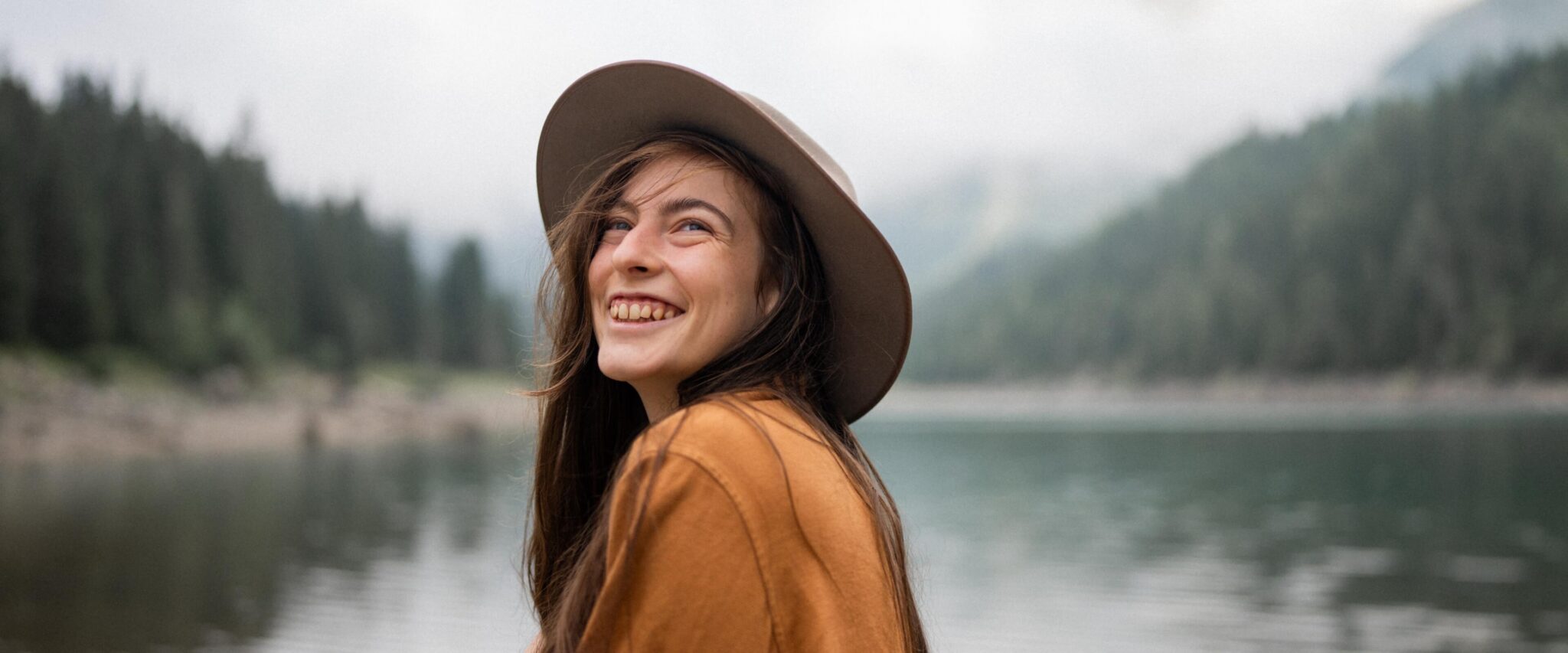 Portrait of photographer Caro by a lake, smiling while while looking up