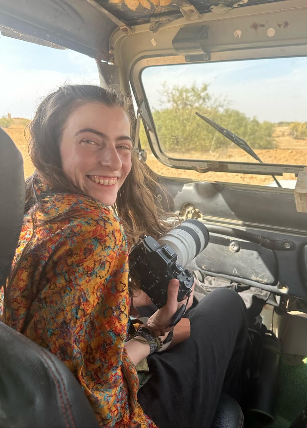 Photographer Caro sitting in a safari truck holding her camera and smiling widely