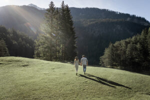 Couple walking hand in hand across a wide meadow in morning light