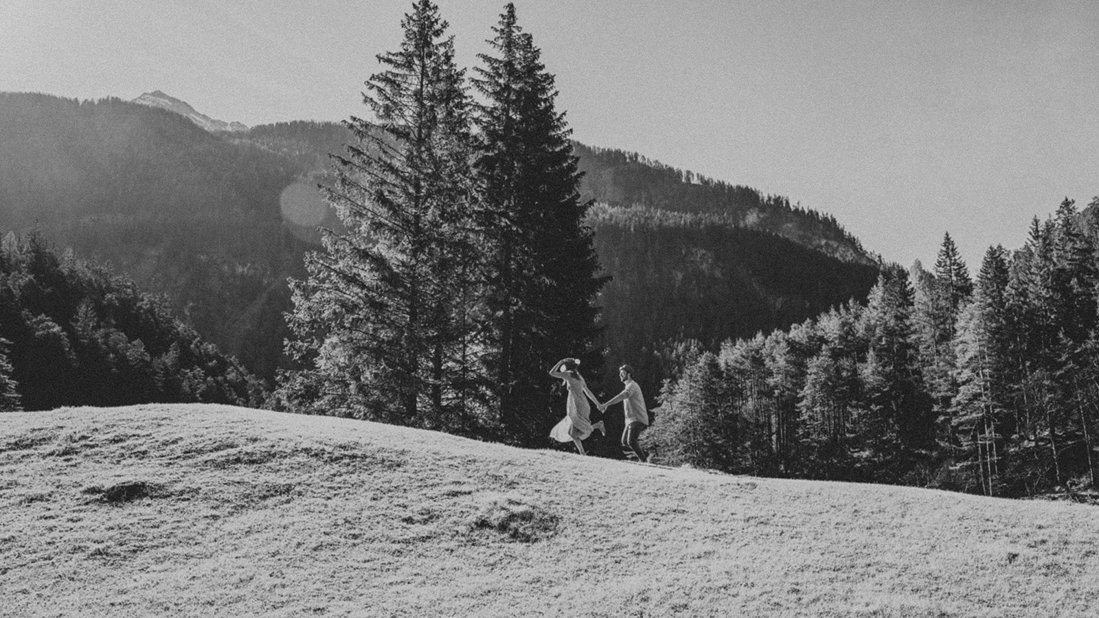 Blurry grainy black-and-white photo of a couple running across a meadow in morning light