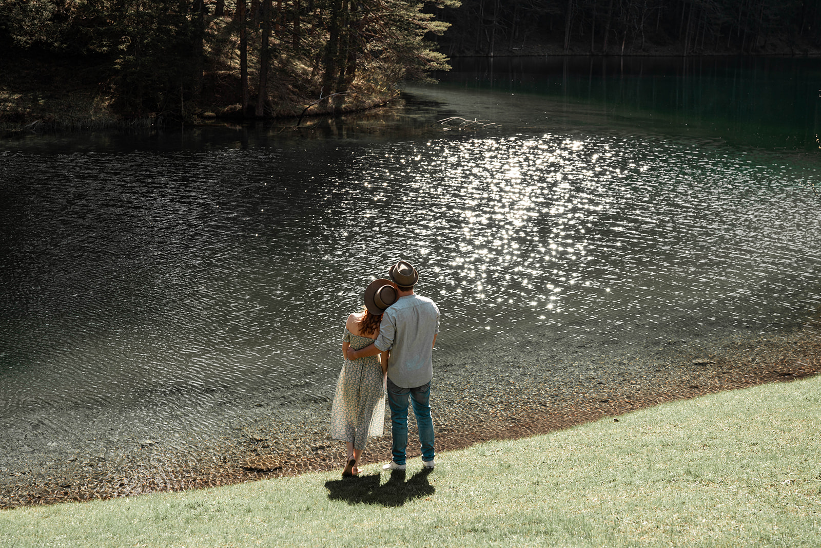 Distant photo of a couple standing together by a lake while gazing into the distance