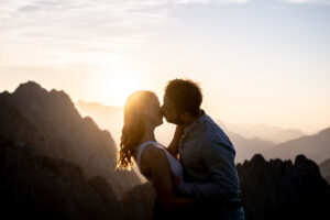 Engaged couple kissing at sunset with mountain silhouettes in the background