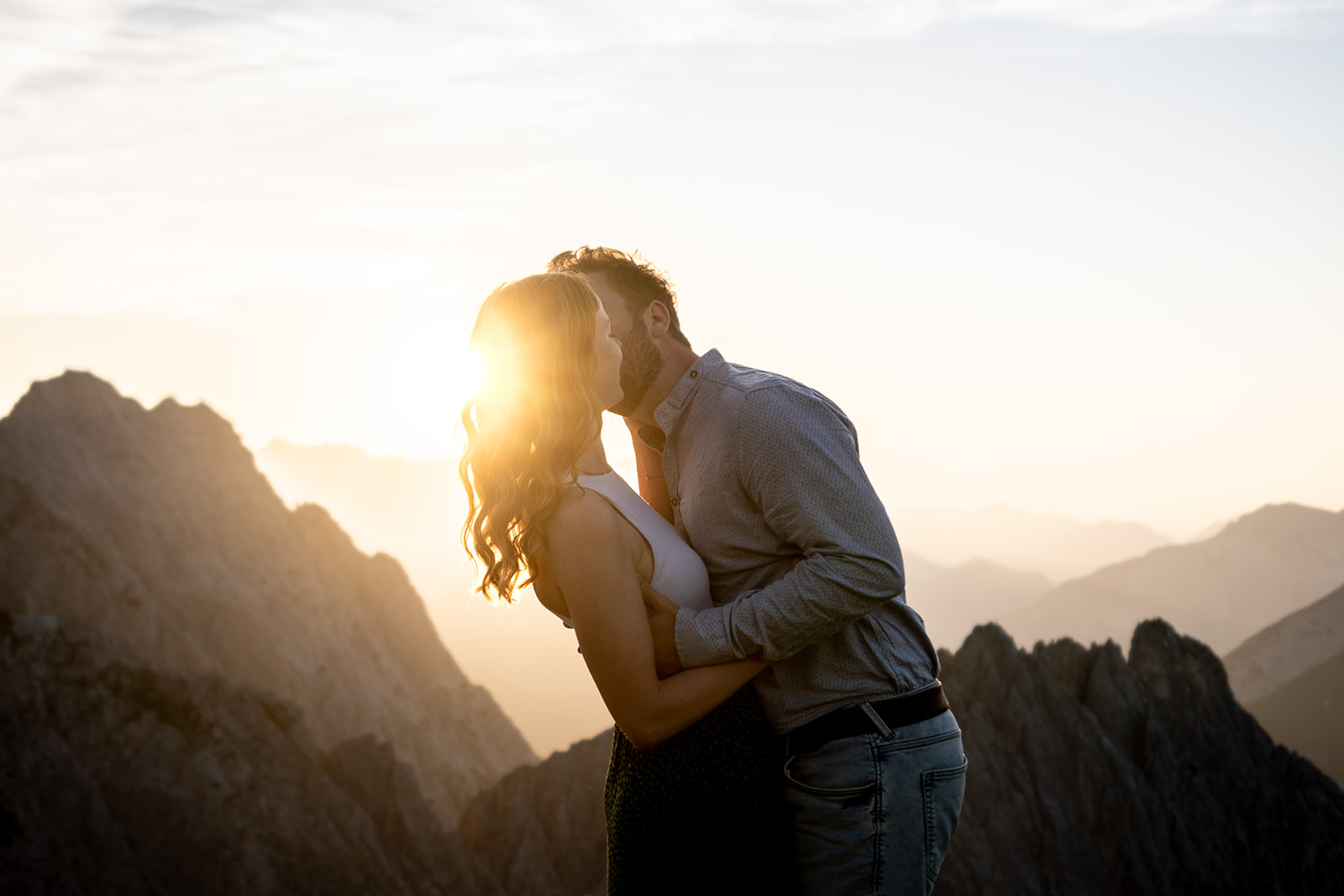 Engaged couple kissing at sunset on a mountain peak