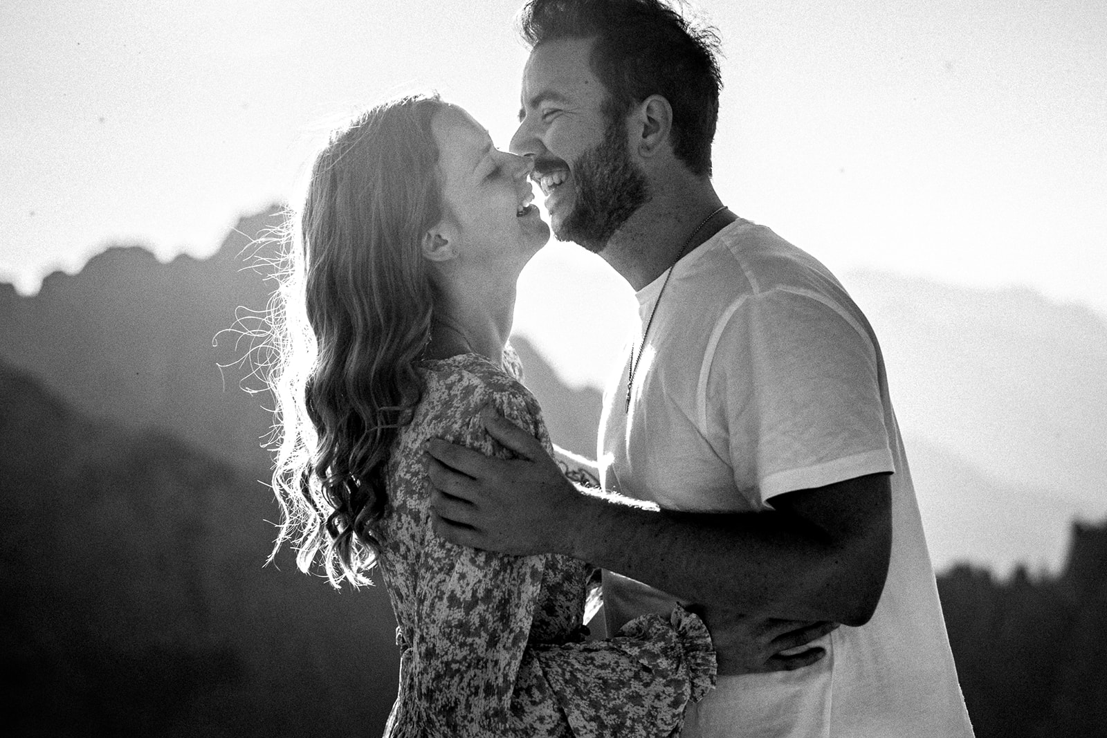 Grainy black-and-white photo of a man whispering into his fiancée’s ear while both laugh