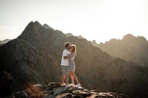 Evening atmosphere in the Tyrolean Alps with a couple standing on a rock while the man whispers into his fiancée’s ear