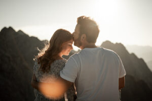 Man kissing his fiancée on the forehead at sunset in the mountains