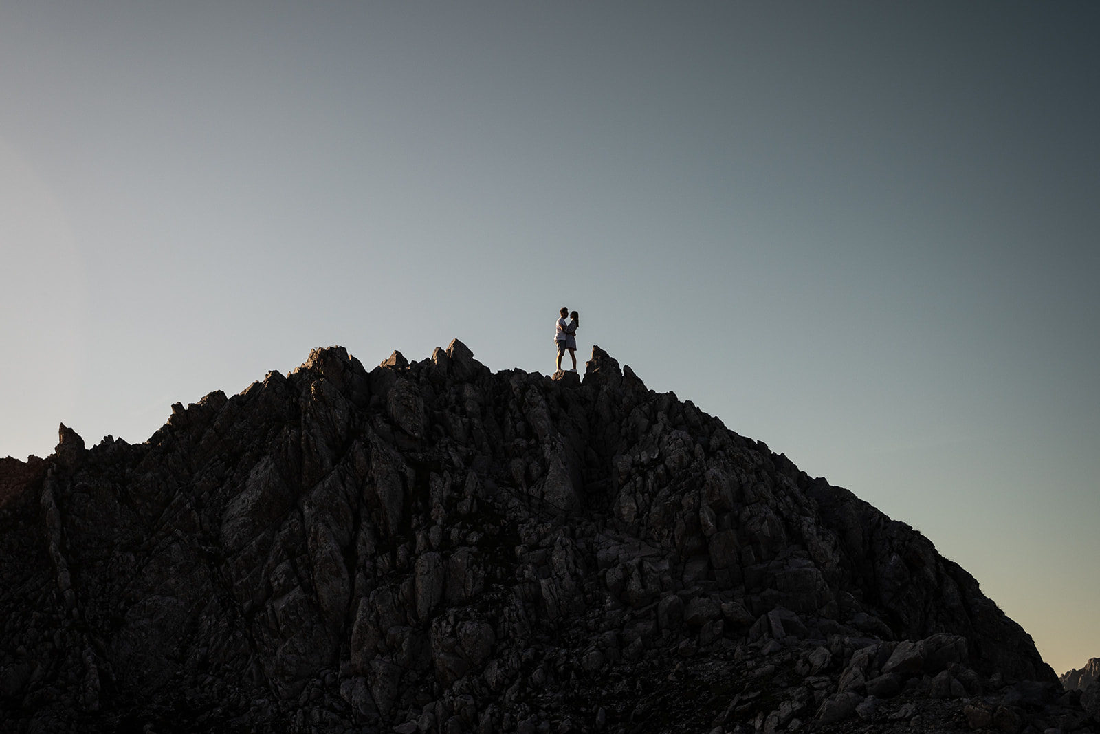 Silhouette photo of a couple leaning against each other on a rocky mountain