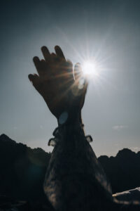 Vintage blurry grainy photo of hands touching beside the sun with mountains in the background