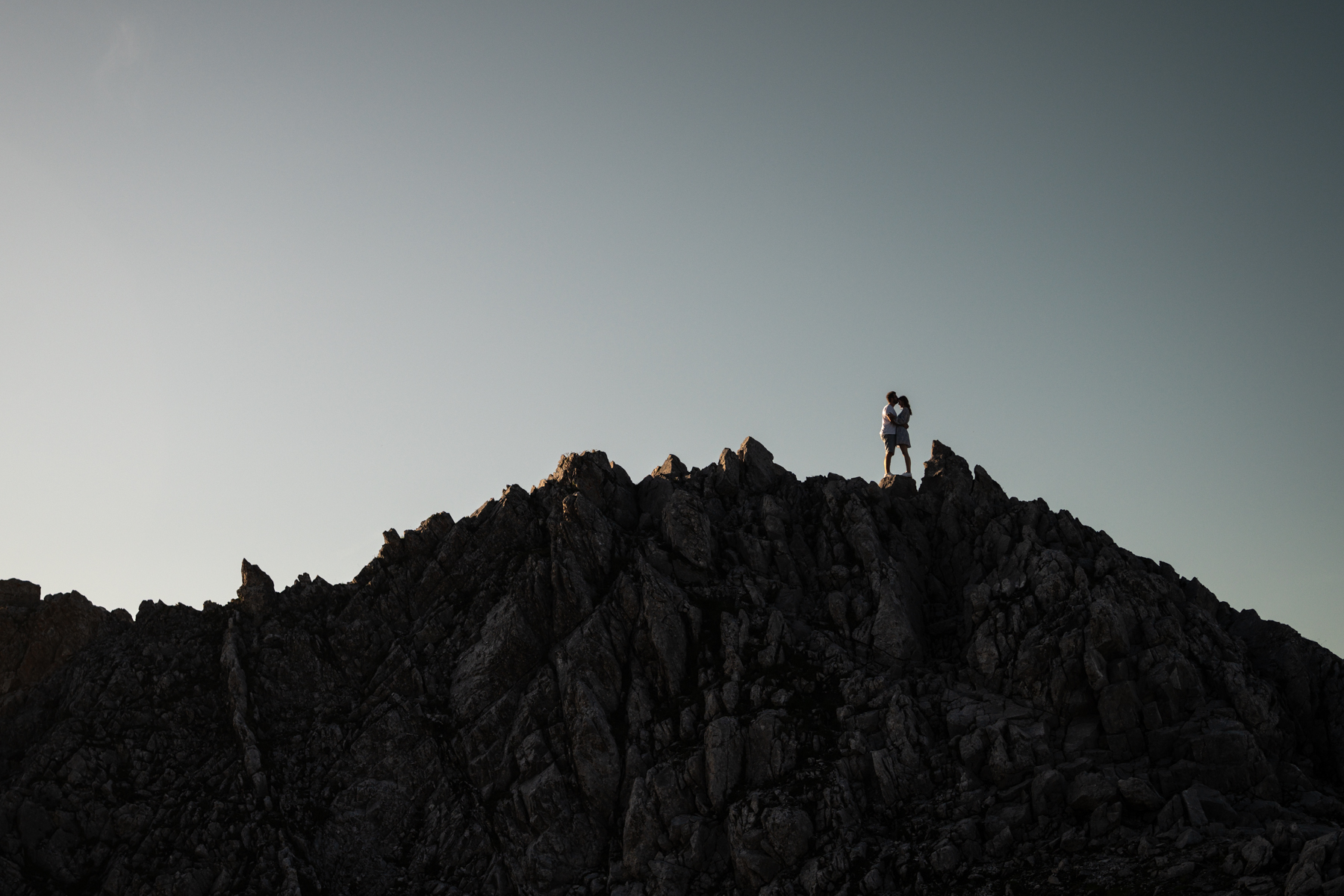 Silhouette of a couple standing on a mountain rock with their heads leaning together