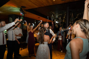The wedding couple dances while guests raise their hands in the background