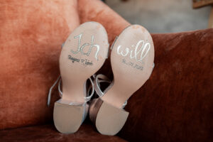 Soles of the bride’s wedding shoes featuring “I do,” the wedding date, and names