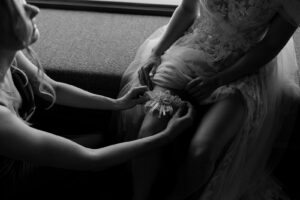 Black-and-white close-up of the bride’s and maid of honor’s hands putting on the garter