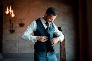 The groom buttons his waistcoat while looking down