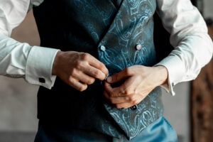 Close-up of the groom’s hands fastening his waistcoat
