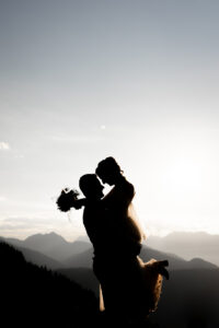 Silhouette of the groom lifting his bride against a mountain sunset