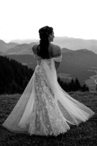 Black-and-white photo of a bride twirling in her dress against a mountain backdrop