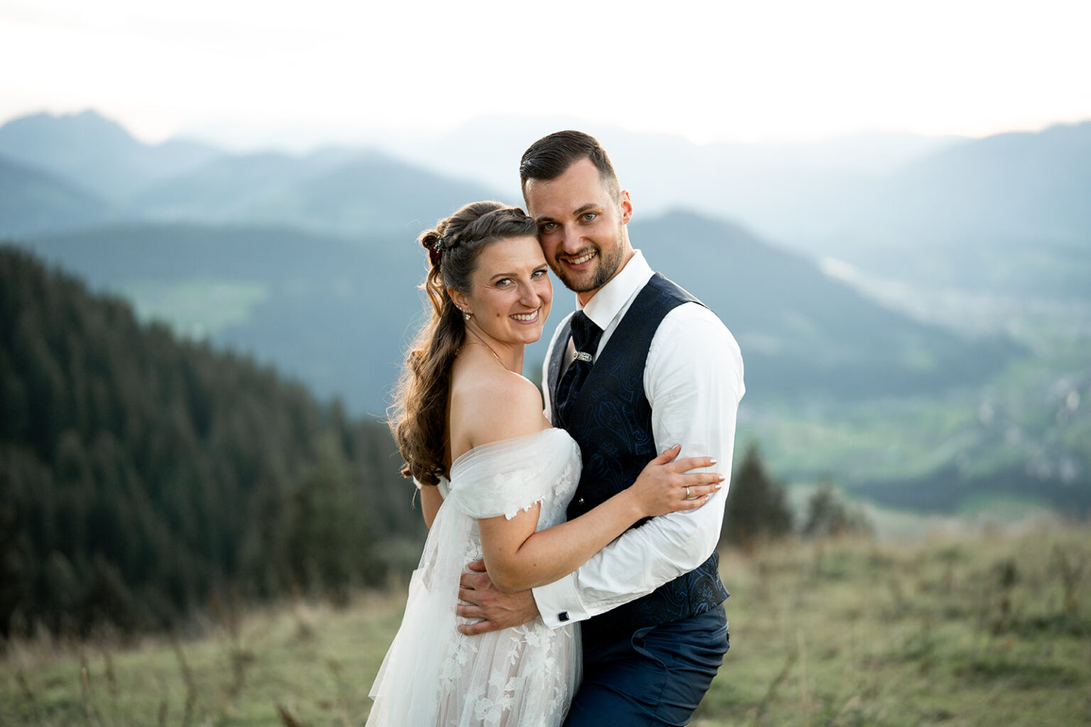Happy wedding couple embracing at sunset in the mountains and laughing at the camera