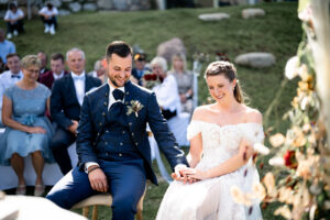 The wedding couple sits hand in hand during the ceremony, smiling down