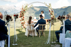 The wedding couple sits before the ceremony arch overlooking the mountains of Itter