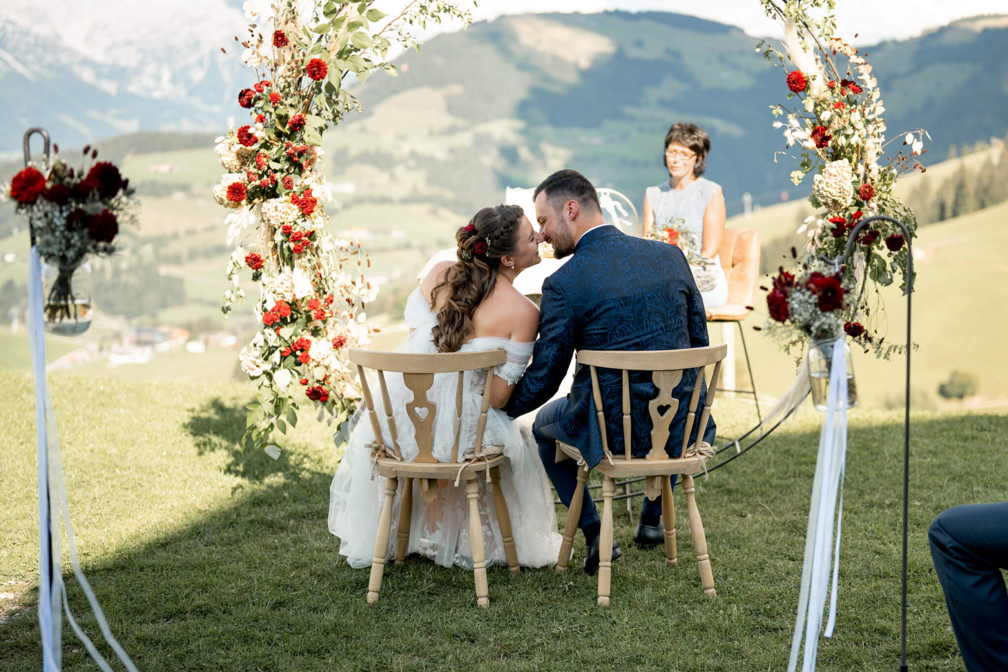Wedding kiss during the ceremony in front of a circular floral arch with mountain views