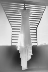 Black and white photo of the full wedding dress hanging from a metal frame