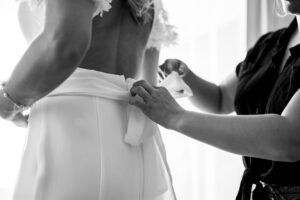 Black and white photo of a bow being tied on the wedding dress