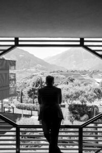 Black and white photo of the groom standing on a balcony looking out at nature