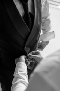 Black and white close-up of the best man's hands fastening the groom's vest
