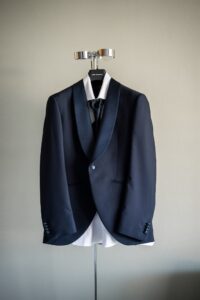 The groom's suit hanging on a hook against a grey-green wall