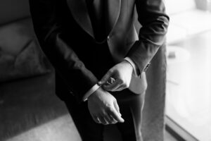 Black and white close-up of the groom adjusting his shirt and jacket