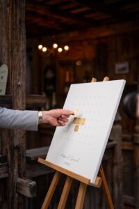 Close-up of a hand attaching a golden plaque to a wedding guest book canvas