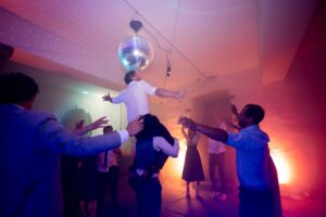 Groom lifted on a guest's shoulders toward the disco ball