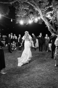 Bride running toward celebrating guests while string lights illuminate the field