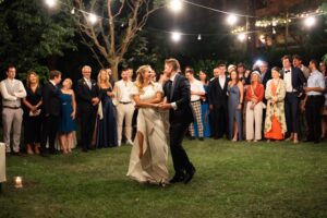 Bride and groom dancing beneath string lights in front of their wedding guests