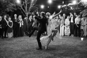 Black and white photo of the bride and groom dancing with raised hands toward their guests