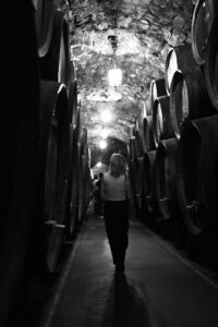 Black and white photo of a woman walking between wine barrels in a historic cellar