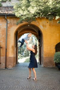 Young woman joyfully tossing a boy into the air in front of a historic archway in the courtyard
