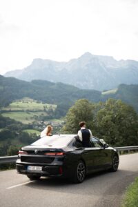 Wedding couple sitting on the window frame of a moving car in the mountains